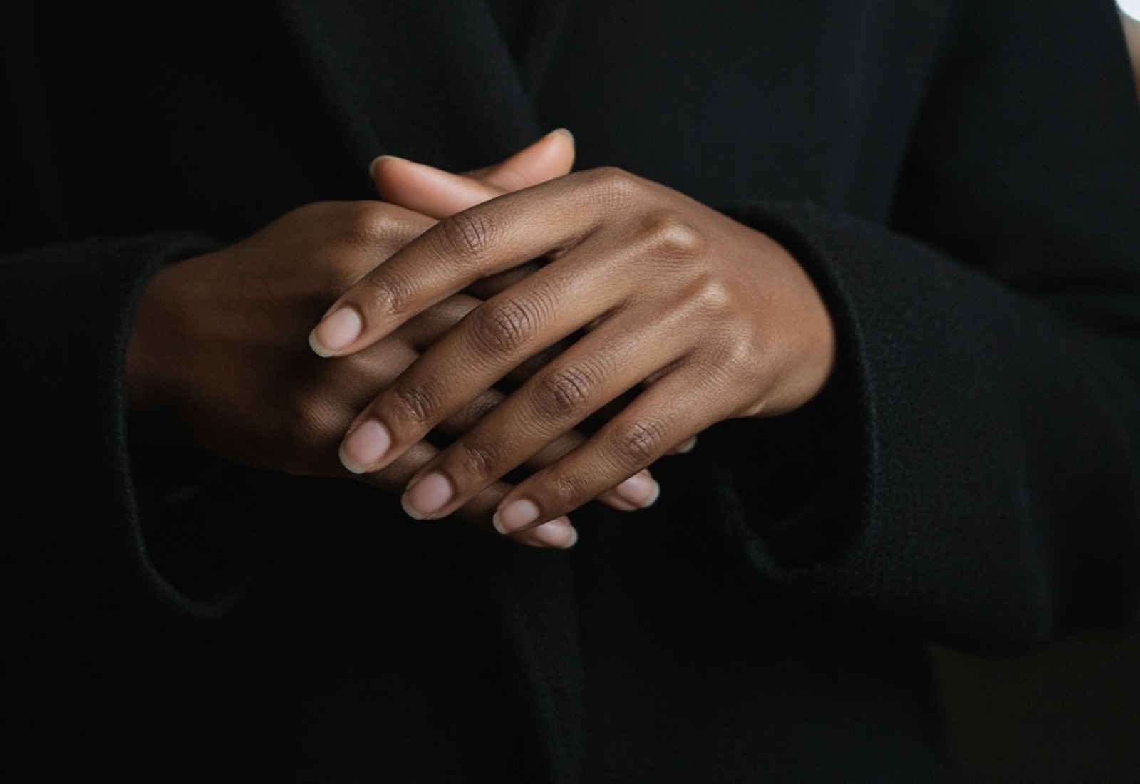 A woman’s hands held together against a dark city night